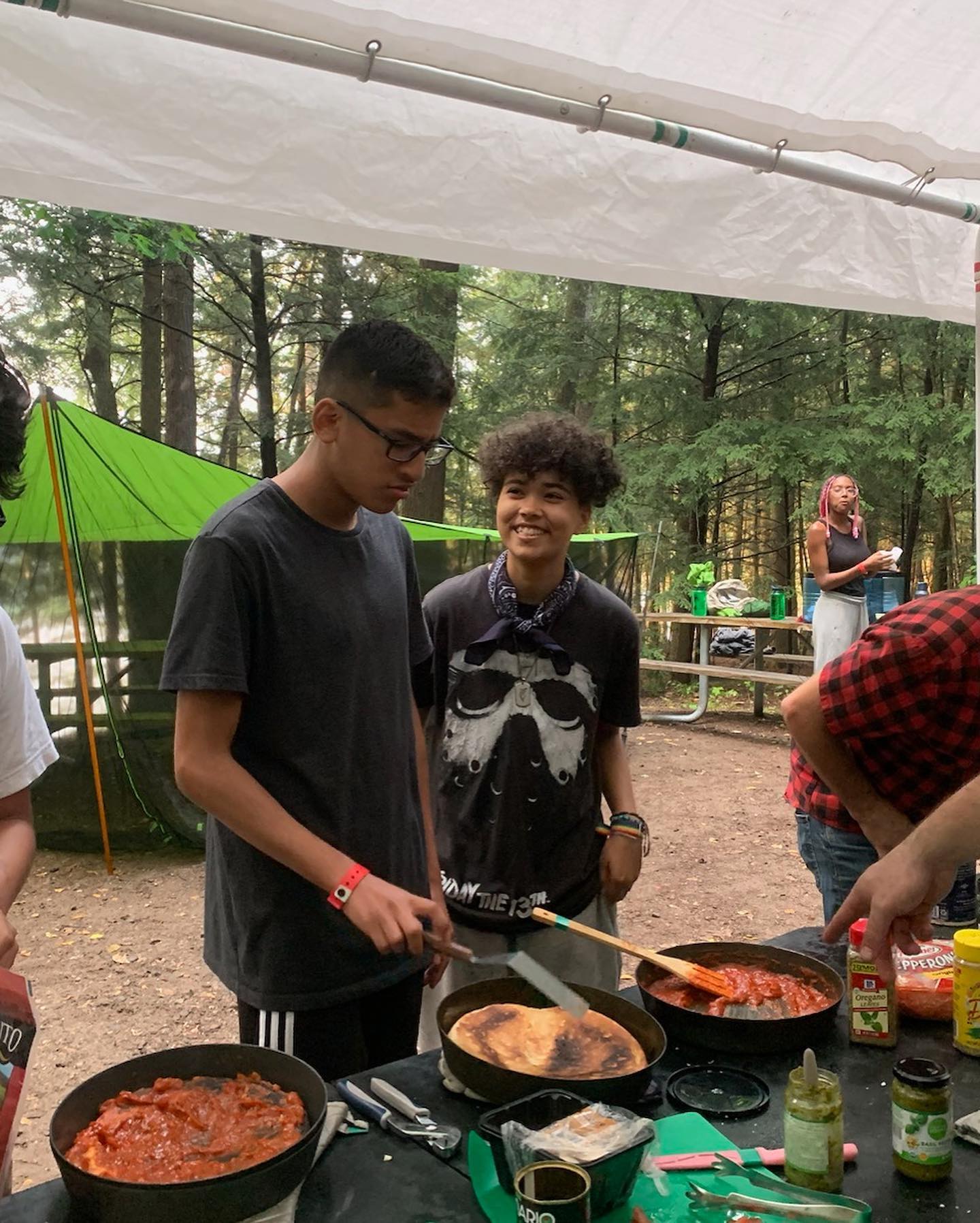 Young people cooking a meal over camp stoves and dutch ovens under the tarp kitchen at a hosted basecamp