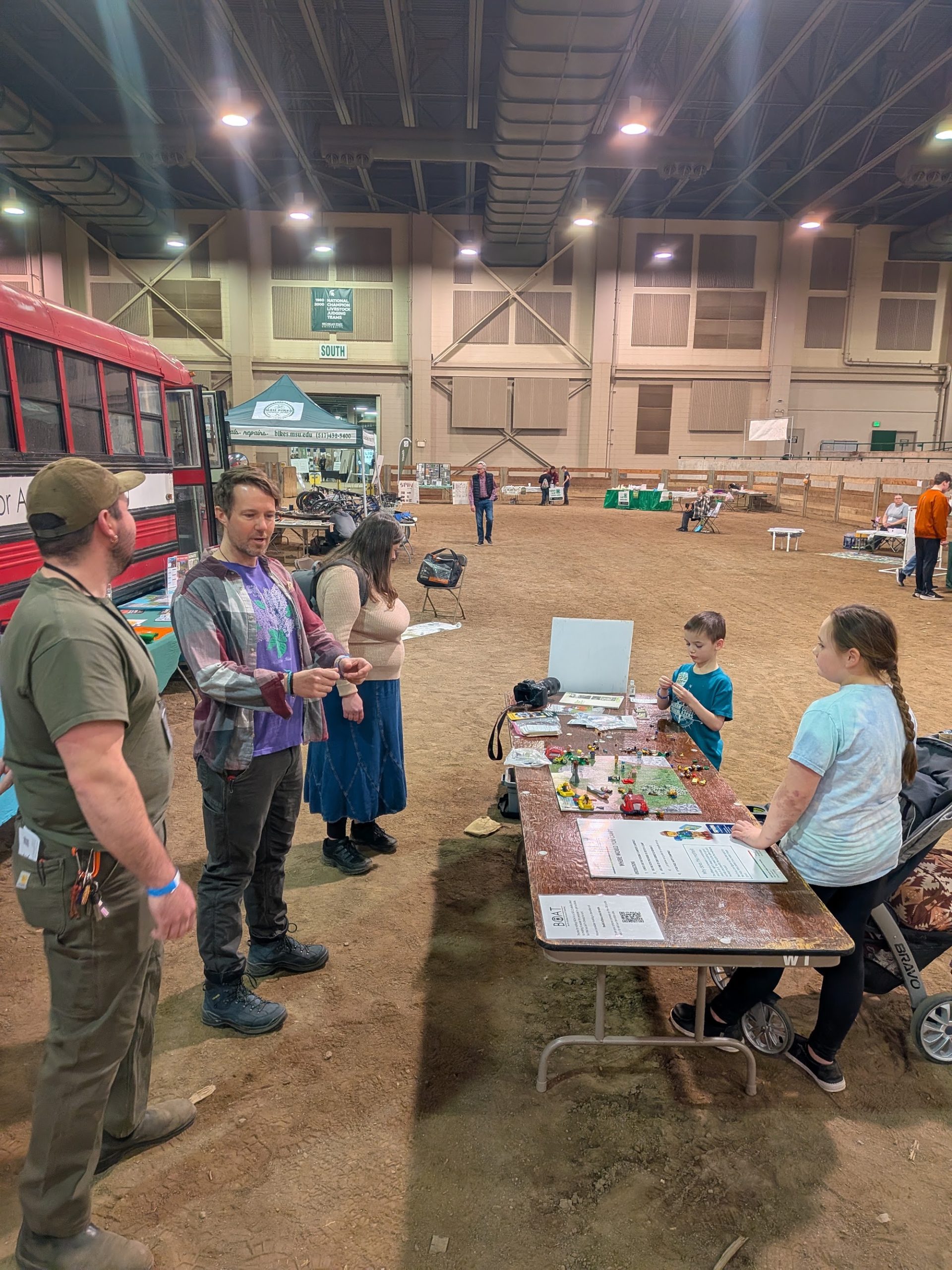 A Get Outside Coach talks with event attendees while children work through a hands-on activity at the bus-side table