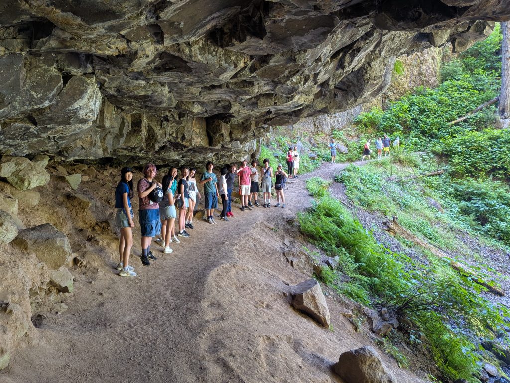 Lewis & Clark camp participants hiking single file beneath a mossy rock overhang