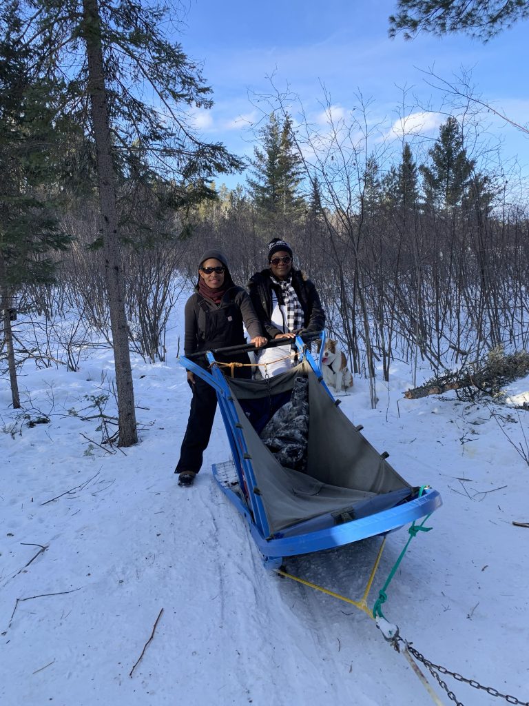 An Outdoor Afro participant riding a dog sled along a snowy trail in Minnesota